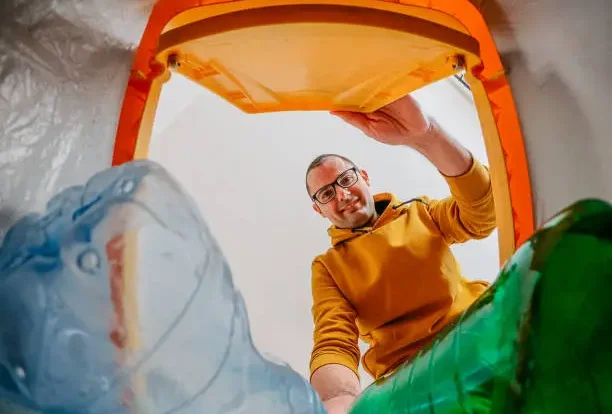 Homme souriant jetant une bouteille en plastique dans une poubelle de tri sélectif