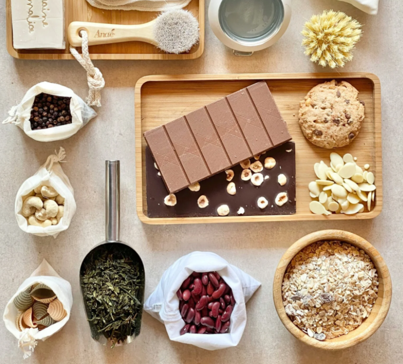 Produits en vrac zéro déchet : savon, brosse, chocolat, fruits secs et accessoires réutilisables sur fond clair.